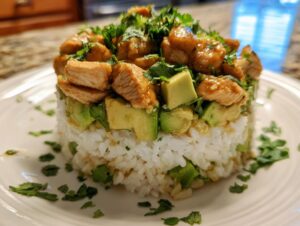 A perfectly plated honey lime chicken & avocado rice stack featuring layers of white rice, avocado chunks, and glazed chicken, topped with cilantro.