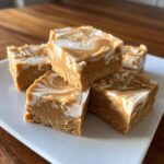 Close-up of several squares of keto peanut butter vanilla swirl fudge stacked on a white plate.