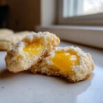 A lemon lavender thumbprint cookie broken in half showing the bright yellow lemon curd filling inside.