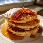 A tall stack of fluffy maple ginger pancakes being drizzled with golden syrup.