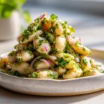 A mound of vibrant marinated white bean salad mixed with fresh parsley and slivers of red onion on a speckled plate.