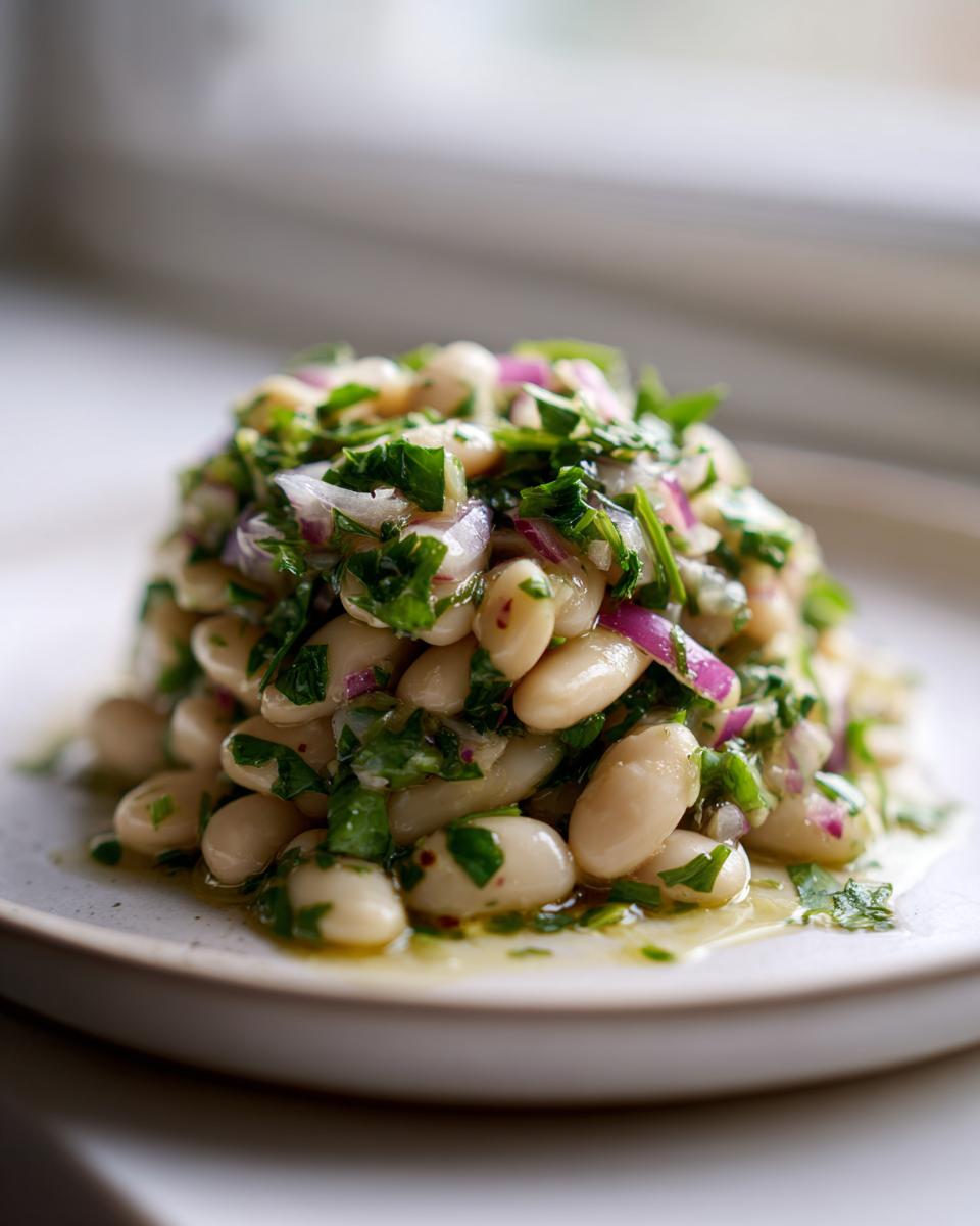 A mound of marinated white bean salad mixed with chopped red onion and fresh parsley, glistening with dressing.