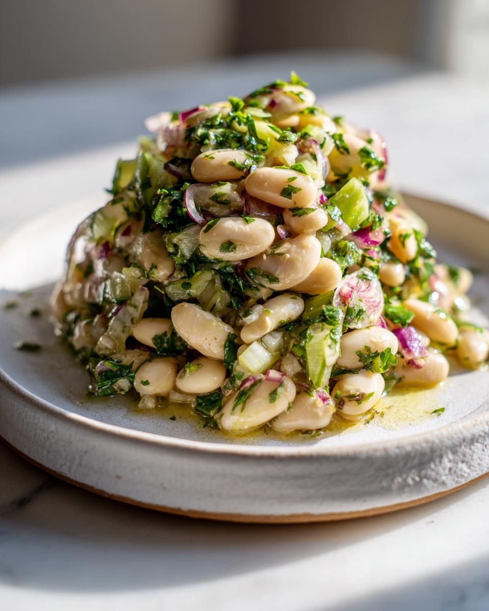A mound of vibrant marinated white bean salad featuring cannellini beans, red onion, celery, and fresh parsley, glistening with dressing.