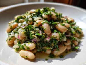 A close-up of a vibrant marinated white bean salad featuring cannellini beans, chopped red onion, and fresh green herbs.