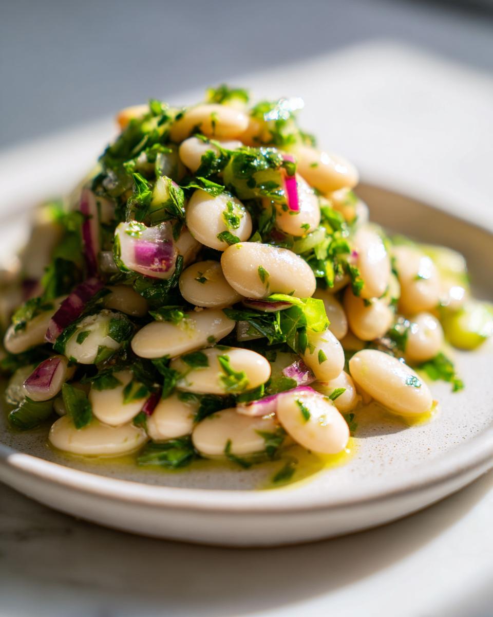A close-up serving of marinated white bean salad featuring cannellini beans, chopped red onion, and fresh green herbs drizzled with oil.