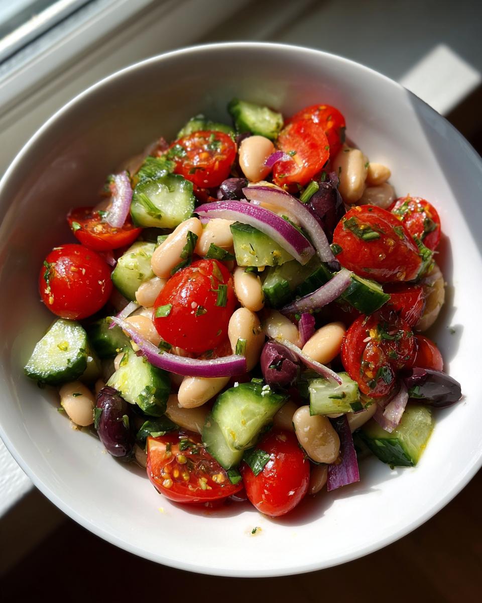 Close-up of a vibrant mediterranean white bean salad featuring white beans, cherry tomatoes, cucumber, and red onion.