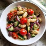 Close-up of a bright mediterranean white bean salad featuring cannellini beans, cherry tomatoes, cucumbers, olives, and red onion.