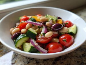 A vibrant bowl of mediterranean white bean salad featuring white beans, cherry tomatoes, cucumber, red onion, and Kalamata olives.
