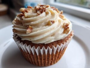 Close-up of a moist banana walnut cupcake topped with a swirl of cream cheese frosting and chopped walnuts.