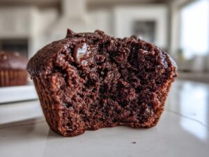 Close-up of a rich, dark chocolate muffin cut in half, showing a moist interior and melted chocolate chips.