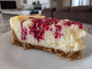 A close-up view of a thick slice of no bake lemon raspberry cheesecake with a graham cracker crust on a white plate.