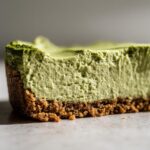 A close-up cross-section of a rich, creamy no-bake matcha cheesecake slice showing the graham cracker crust.