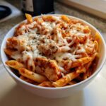 A white bowl filled with one pot chicken parm pasta, topped generously with melted mozzarella cheese and dried herbs.