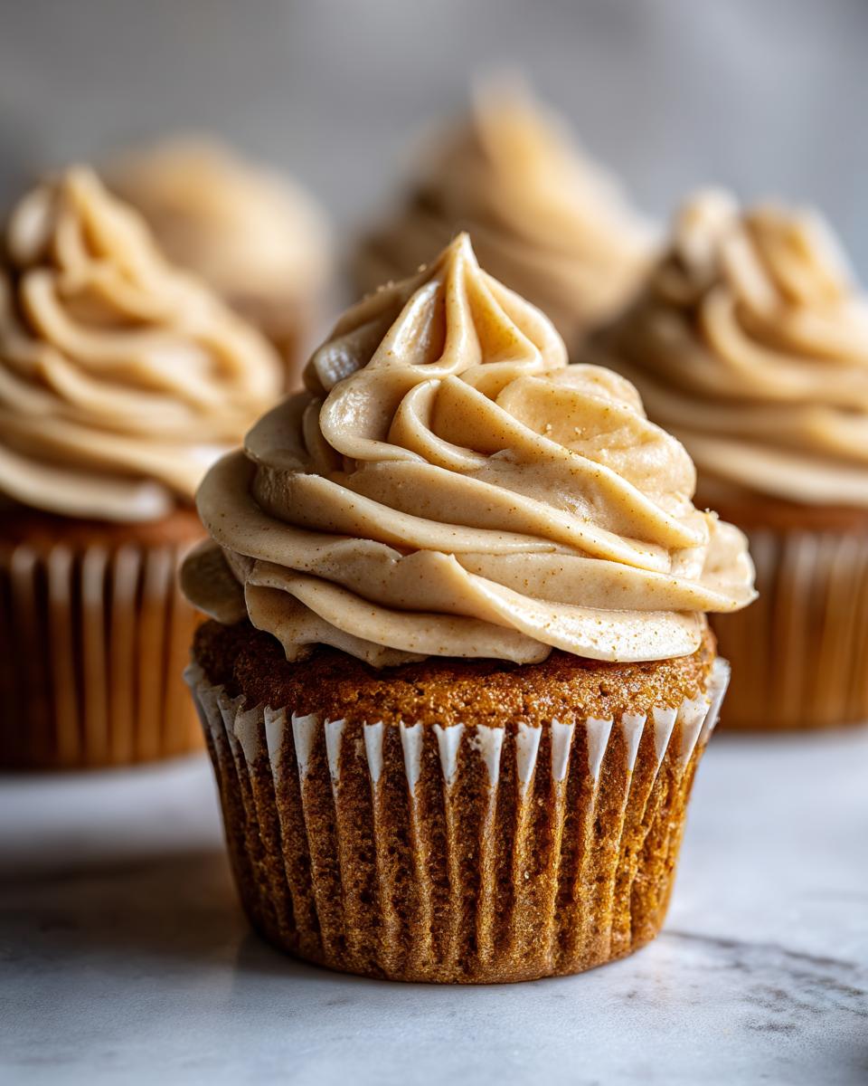 A close-up of one perfectly baked peanut butter banana cupcake topped with a tall swirl of light brown peanut butter frosting.