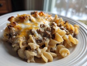 A close-up of a serving of Salisbury steak pasta mixed with creamy sauce and topped with melted, browned cheese.