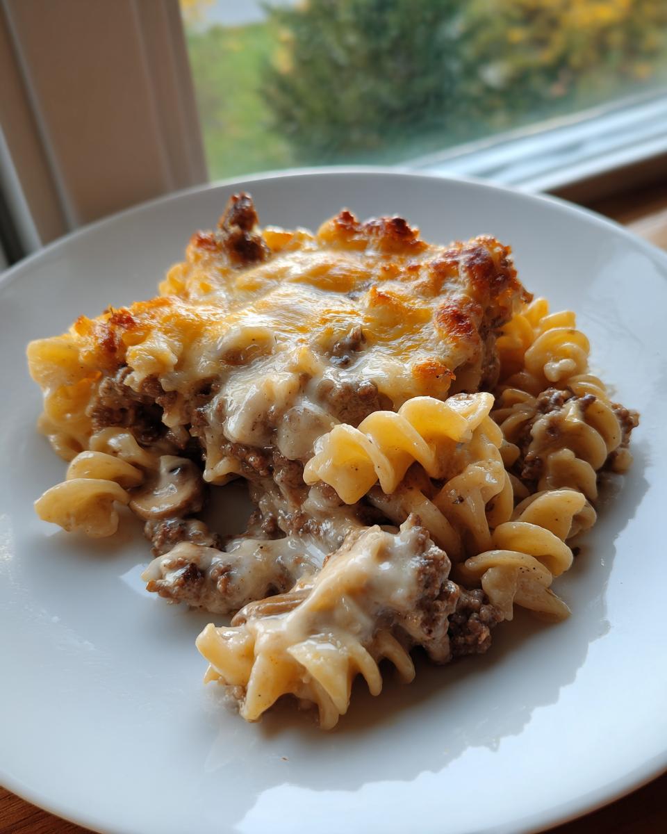 A serving of rich Salisbury steak pasta featuring rotini noodles, ground beef gravy, and a golden, melted cheese topping.