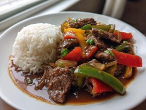 A plate featuring slow cooker pepper steak with colorful bell peppers and onions served next to a mound of white rice.