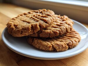 A stack of three golden brown, fork-pressed softest peanut butter cookies resting on a small white plate.