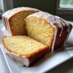 Close-up of a sliced sourdough discard lemon loaf topped with thick white glaze and lemon zest.
