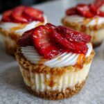 A close-up of a single strawberry cheesecake cupcake topped with whipped cream and glazed strawberry slices.