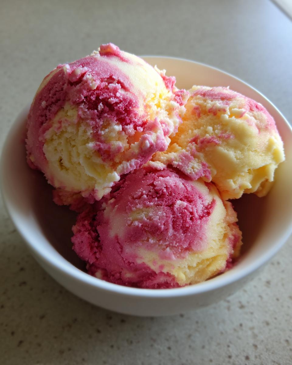 Three scoops of swirled pink and yellow summer sherbet served in a small white bowl.