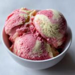 Close-up of three scoops of swirled pink and yellow summer sherbet in a white bowl.
