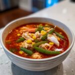Close-up of a white bowl filled with rich, red maryland crab soup loaded with lump crab meat, green beans, and corn.