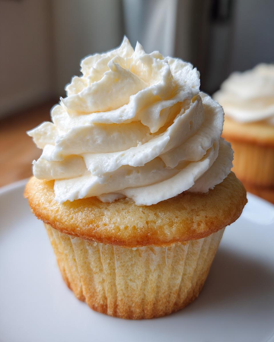 Close-up of a perfectly baked vanilla cupcake from scratch topped with a swirl of white buttercream frosting.