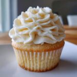 Close-up of a single, perfectly baked vanilla cupcake from scratch topped with a generous swirl of white buttercream frosting.