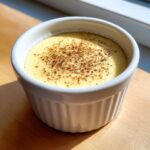 Close-up of a single serving of creamy vanilla custard cups dusted with cinnamon in a white ramekin.