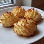 Four perfectly piped and baked vegan duchess potatoes with golden brown, crispy edges served on a white plate.