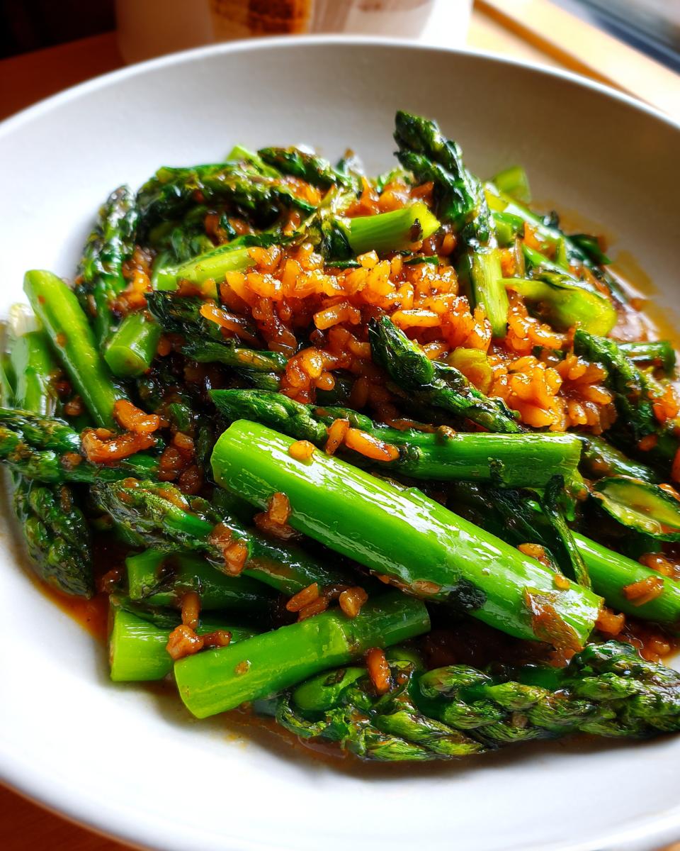 Close-up of bright green asparagus mixed with savory, crispy rice in a white bowl.