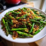 Close-up of vibrant green asparagus mixed with brown, crispy rice served on a white plate.