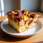 A thick, golden slice of Baked Challah French Toast with a caramelized cinnamon swirl topping on a white plate.