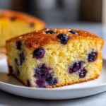 Close-up of a square slice of fluffy blueberry sheet pan pancakes on a white plate.
