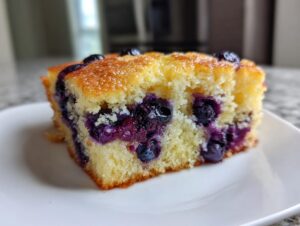 Close-up of a square slice of fluffy blueberry sheet pan pancakes on a white plate.