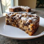 A close-up of a thick slice of Chocolate Chip Cookie Cake topped with white icing.