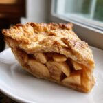 A close-up of a thick slice of Classic apple pie showing tender, spiced apple filling and a golden, flaky top crust.