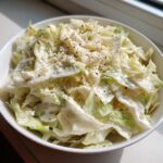 A close-up of creamy Cabbage alfredo tossed in a white bowl and topped with grated cheese and black pepper.