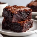 A close-up stack of two incredibly fudgy sweet potato brownies with shiny tops on a white plate.