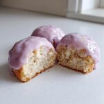 Three Glazed almond mini cakes, one cut open to show the moist interior and thick purple icing.