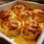 Close-up of golden brown butter swim biscuits soaking in melted butter in a white baking dish.