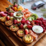 A vibrant Mother's Day brunch grazing board filled with mini quiches, fresh raspberries, strawberries, kiwi, smoked salmon, and dips.