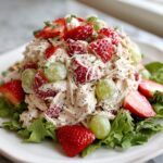 A mound of creamy Panera strawberry poppyseed chicken salad mixed with sliced strawberries and green grapes, served on lettuce.