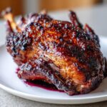 Close-up of a beautifully glazed Roasted half duck with dark, shiny, berry-colored sauce on a white plate.