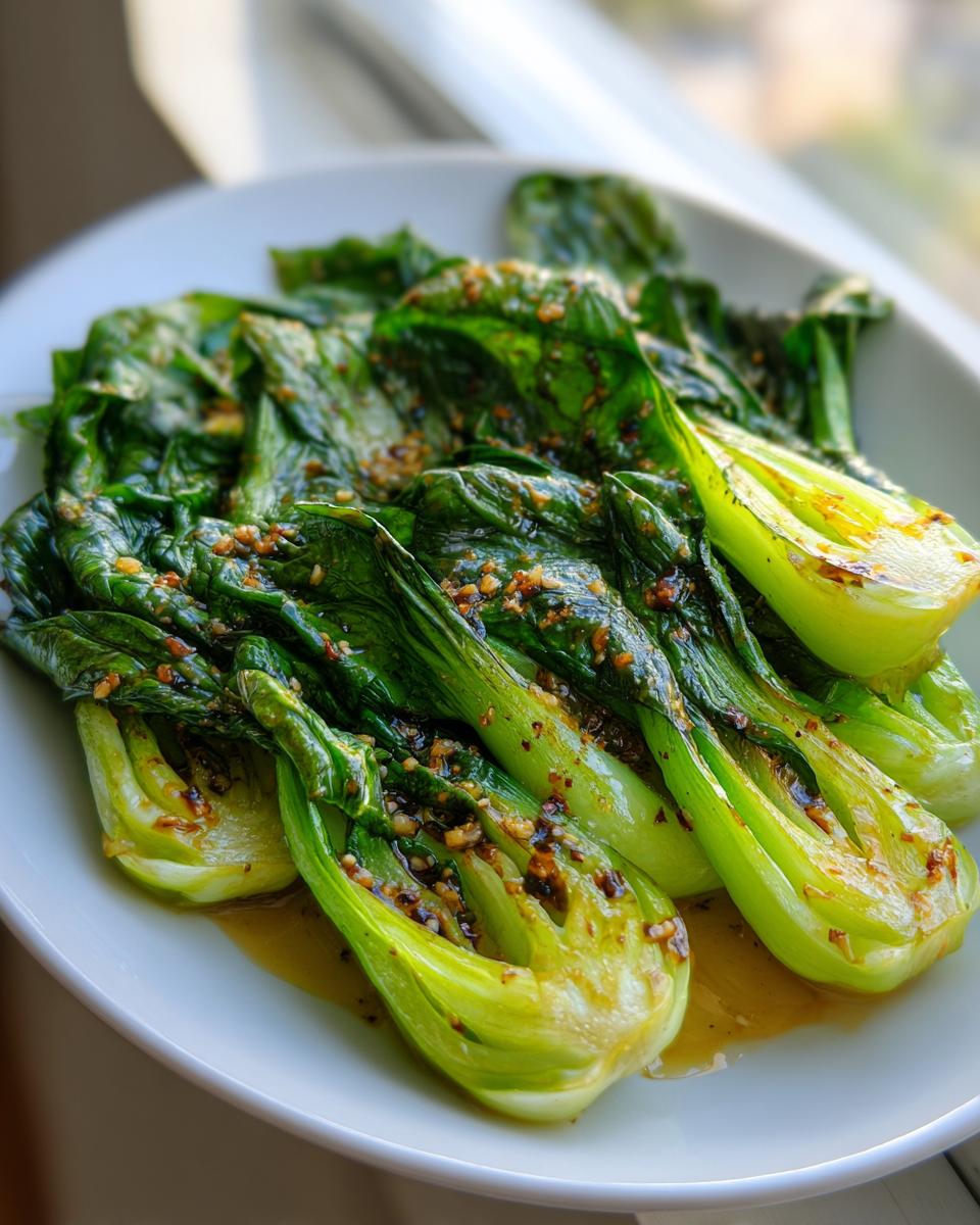 Close-up of vibrant green Sautéed bok choy halves glistening with a savory garlic sauce on a white plate.