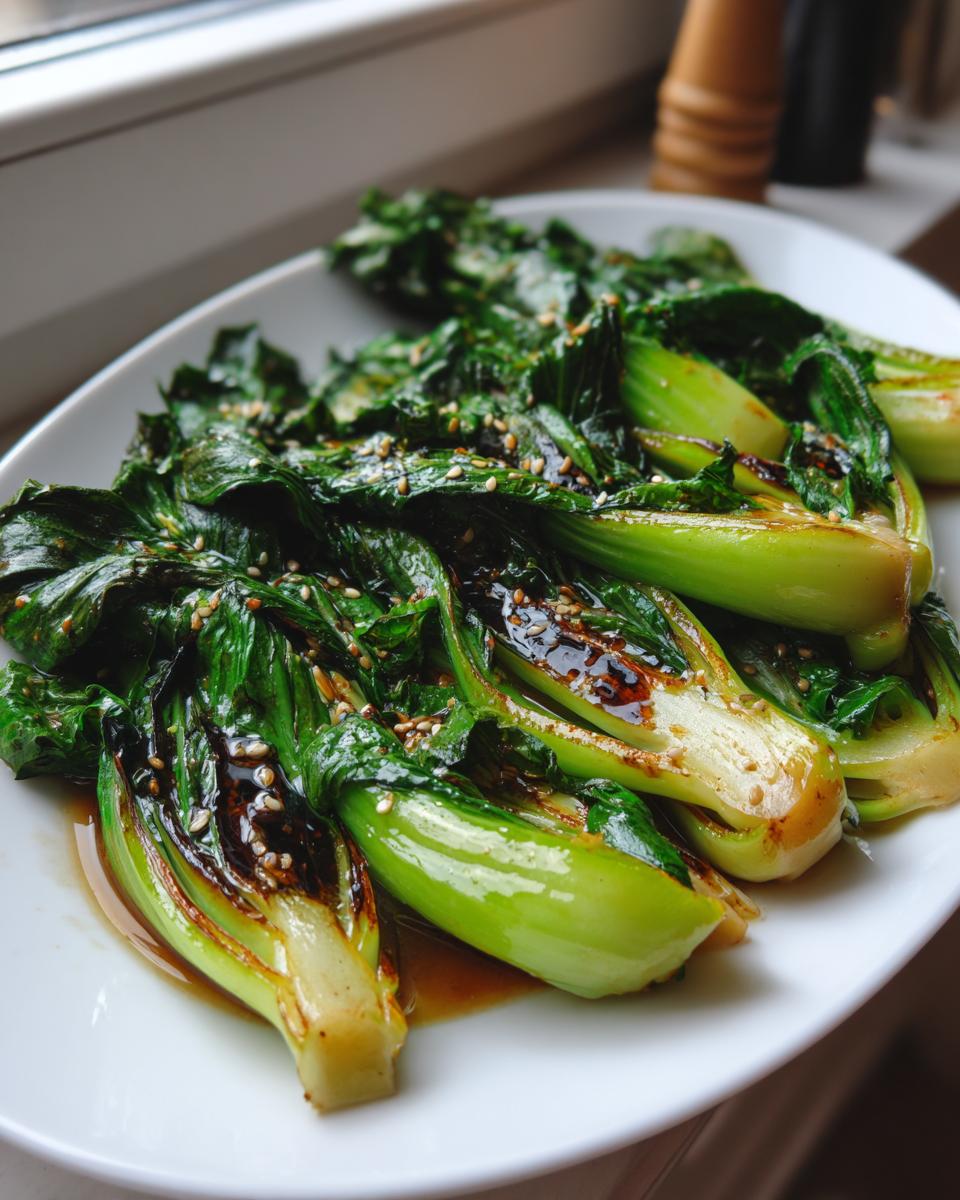 A plate of vibrant, glossy sautéed bok choy drizzled with dark sauce and sprinkled with sesame seeds.