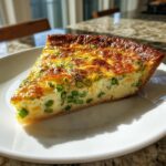 A perfect slice of golden brown Asparagus quiche featuring visible green asparagus pieces in a creamy egg filling.