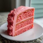 A tall slice of moist Pink lemonade cake showing two layers of pink sponge and pink frosting.