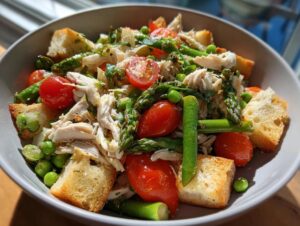 Close-up of a vibrant Spring chicken panzanella salad featuring shredded chicken, cherry tomatoes, asparagus, peas, and croutons.
